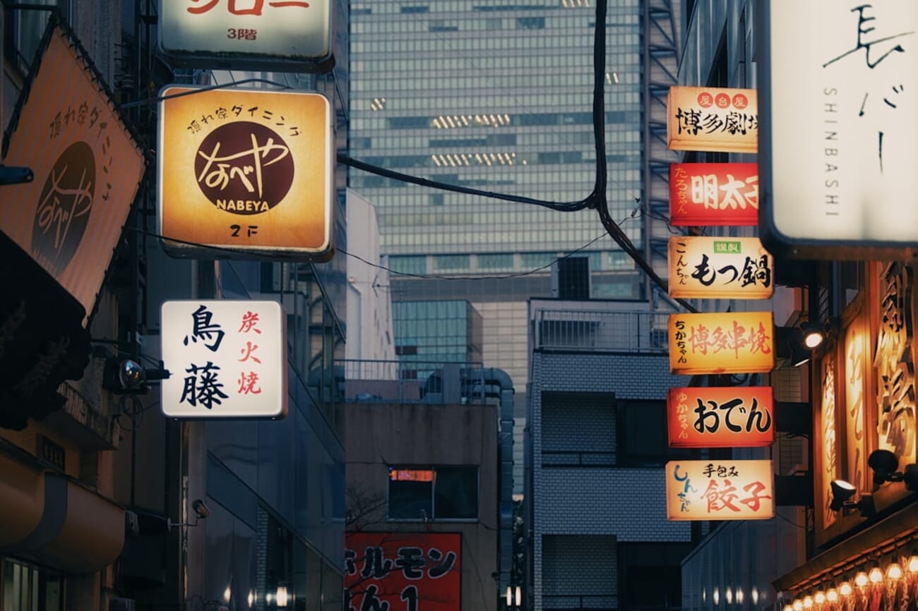 Glowing signs illuminate a narrow city street at dusk — street photography captures authentic moments AI cannot generate