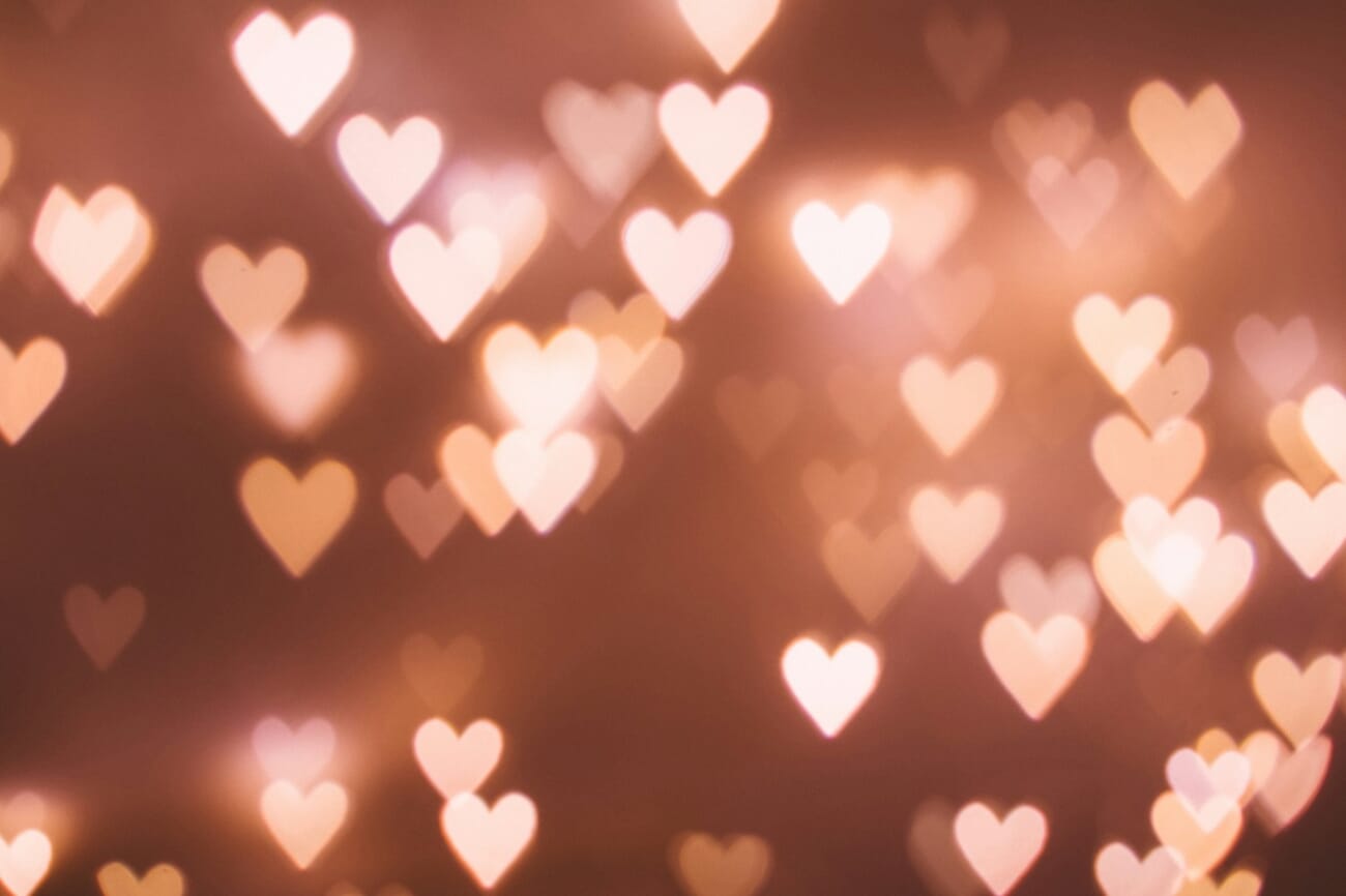 Dozens of heart-shaped bokeh highlights in warm pink and gold, produced by a fast prime with a custom heart-shaped aperture mask.