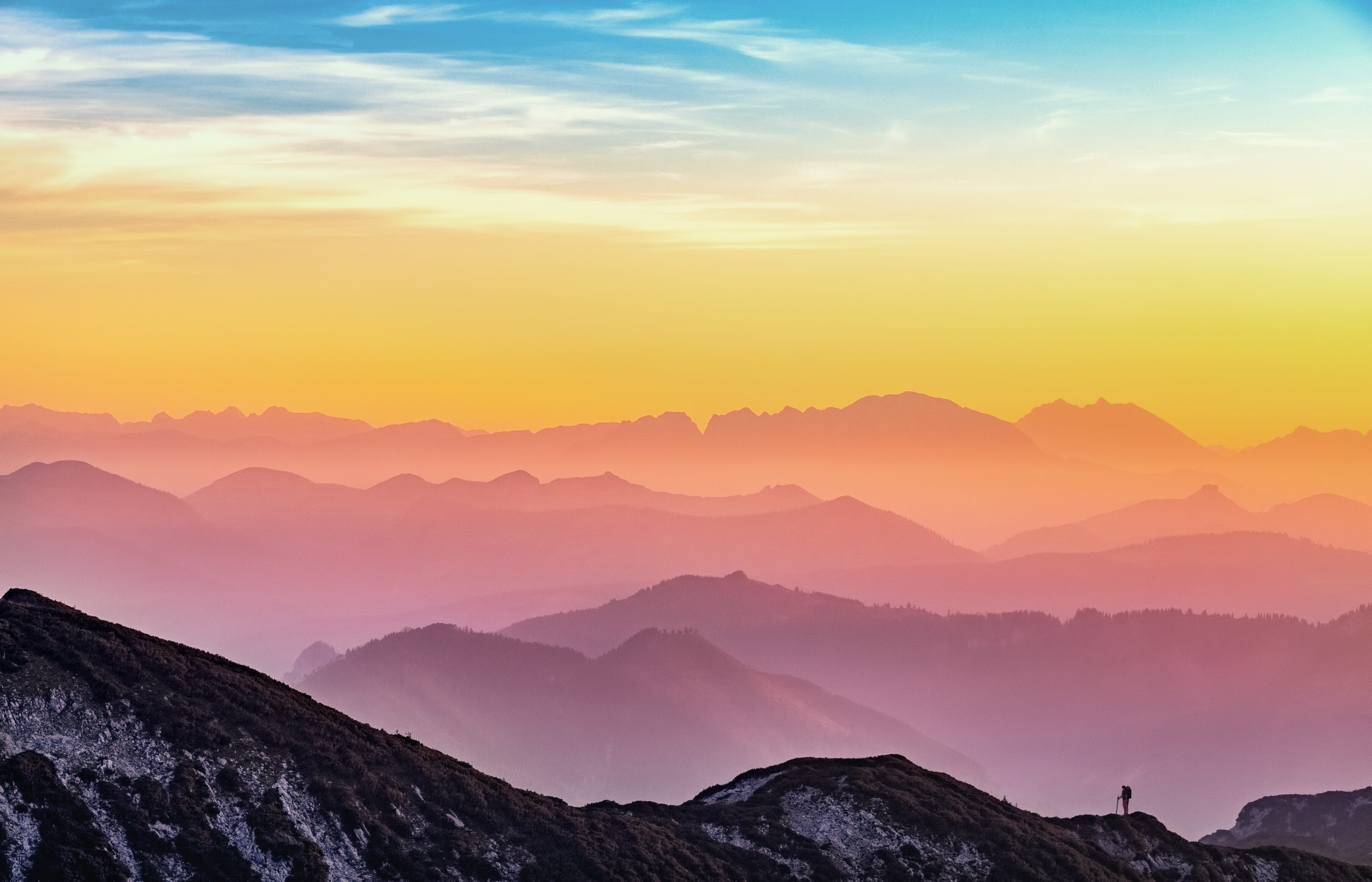 Mountains against the sky at sunset with a tiny figure standing on a ridge.