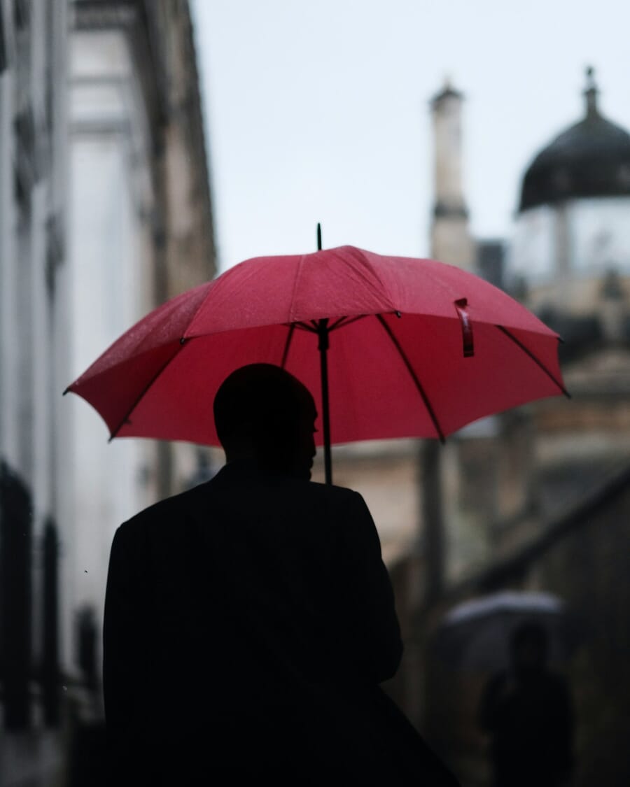 Person with a red umbrella in a muted grey alley, demonstrating the compositional weight of a single saturated color