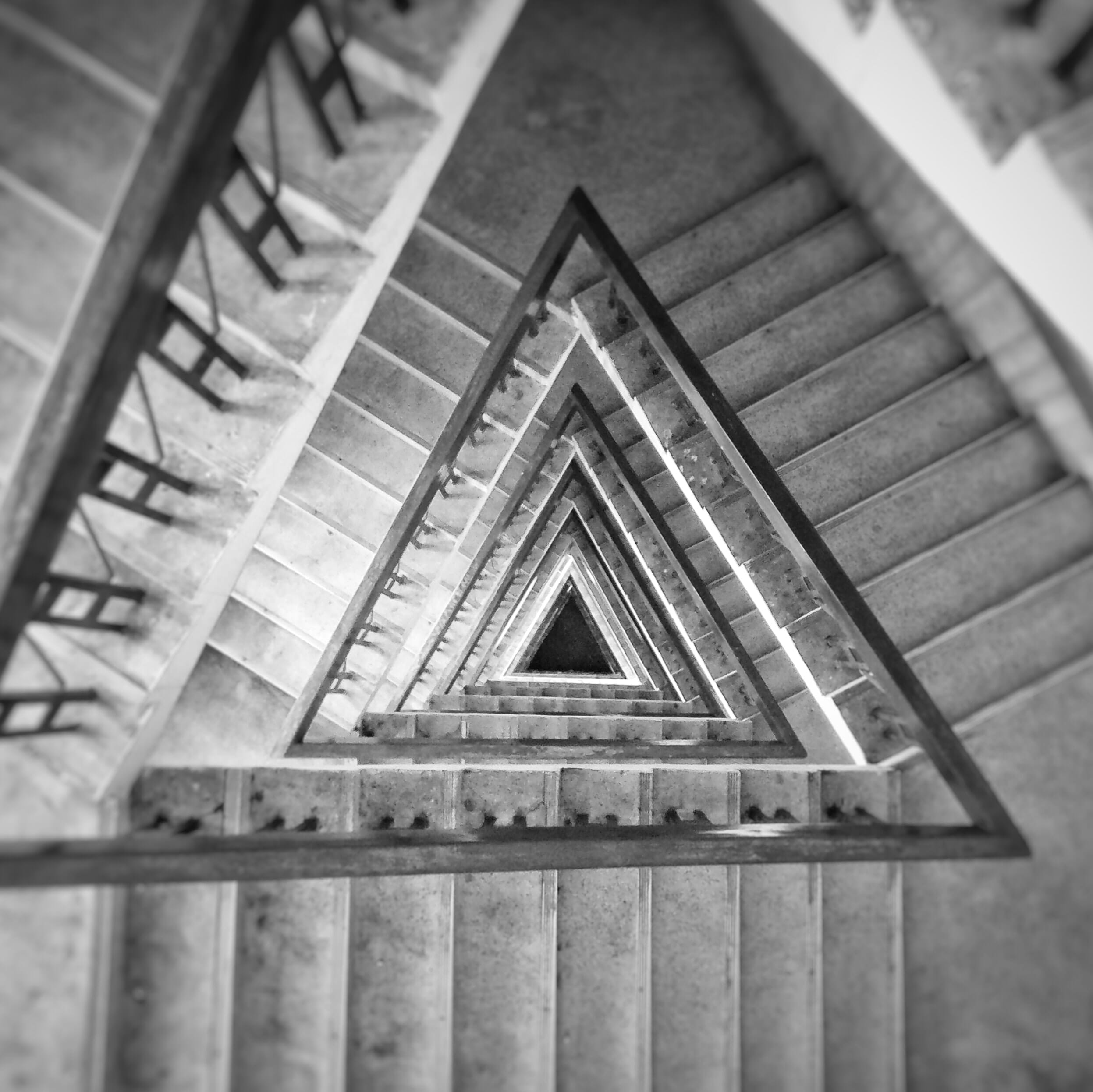 A triangular staircase viewed from above and descending downward in black and white.