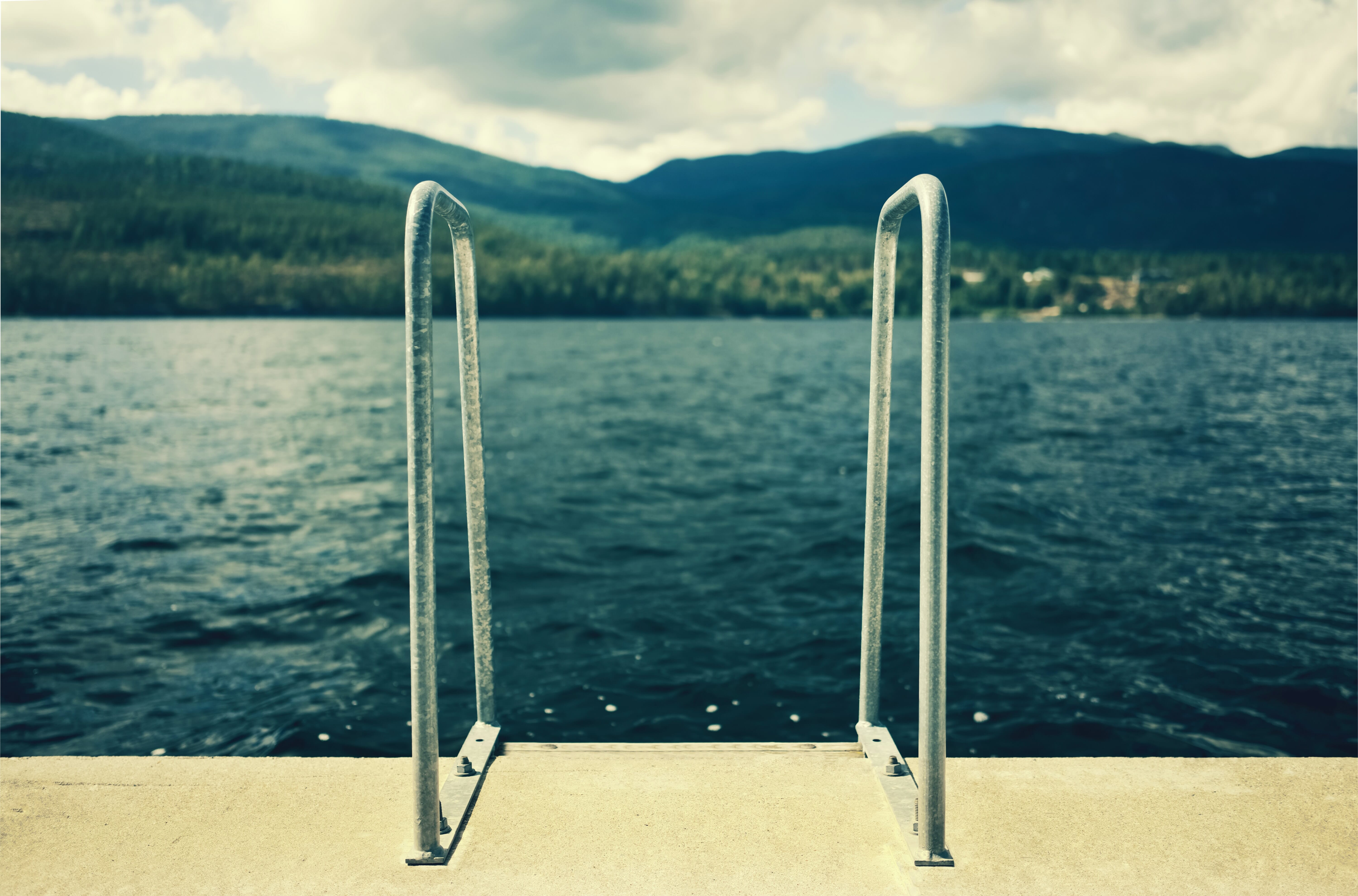 Metal railings sit atop a concrete structure near an ocean with mountains in the background.