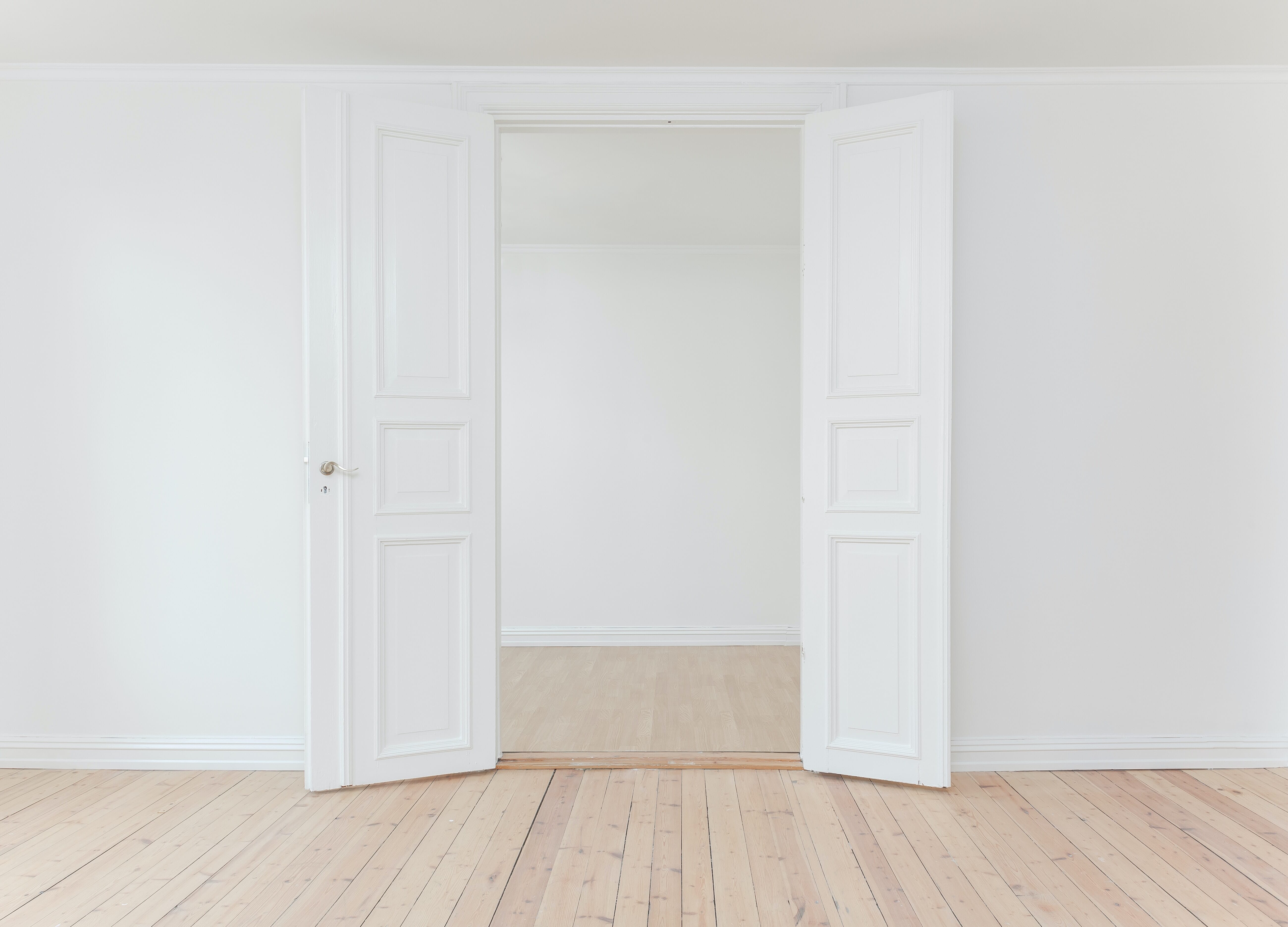 Two white doors open on an apparently empty room with worn wooden floorboards in the foreground.