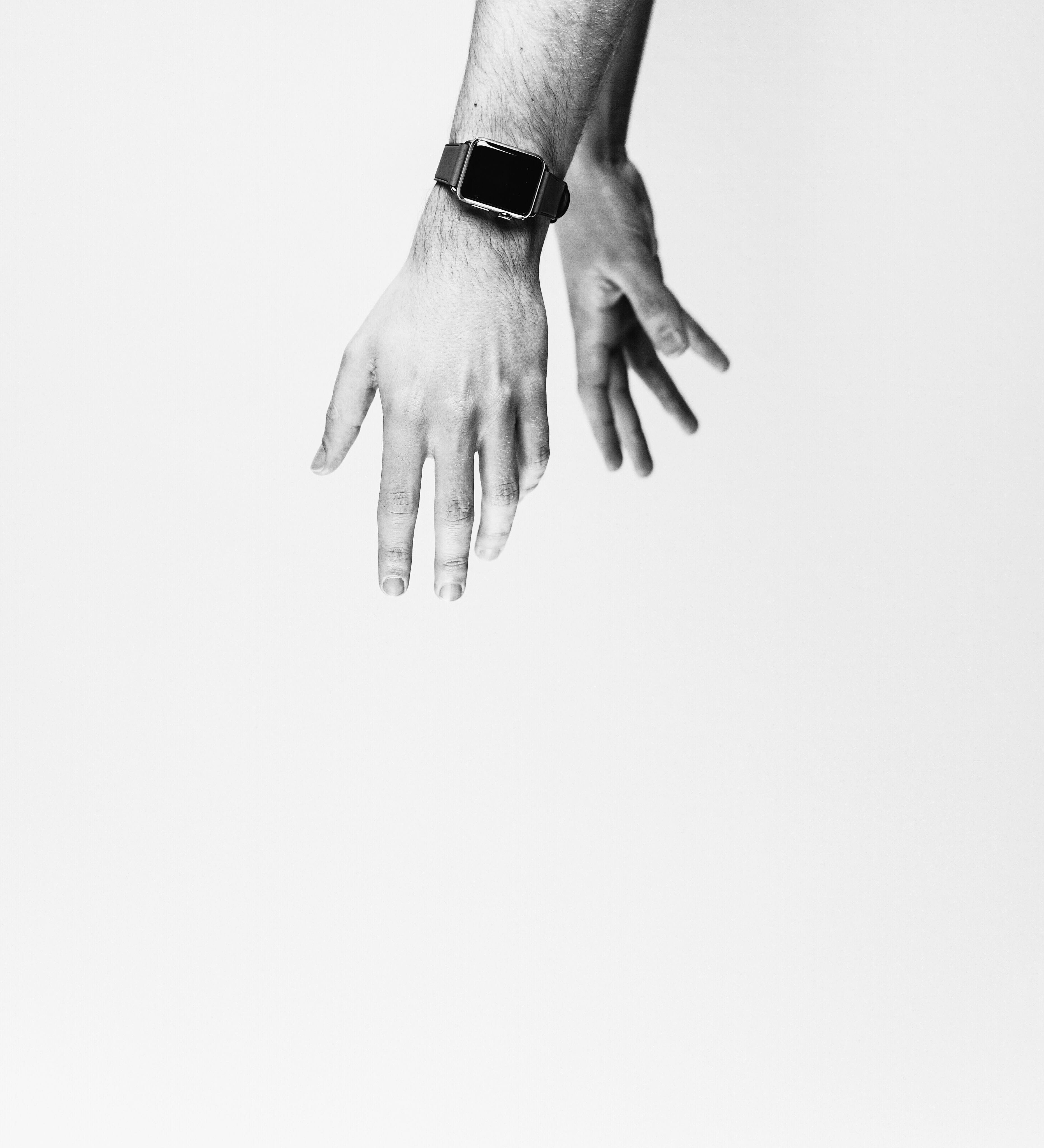 Two hands reaching down toward the bottom of the frame against a light gray background in black and white.