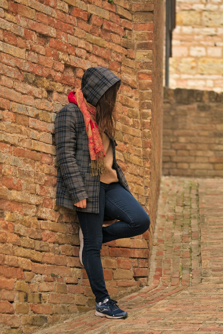Woman leaning against a brick wall with one foot pressed against the wall and the other leg straight on the ground