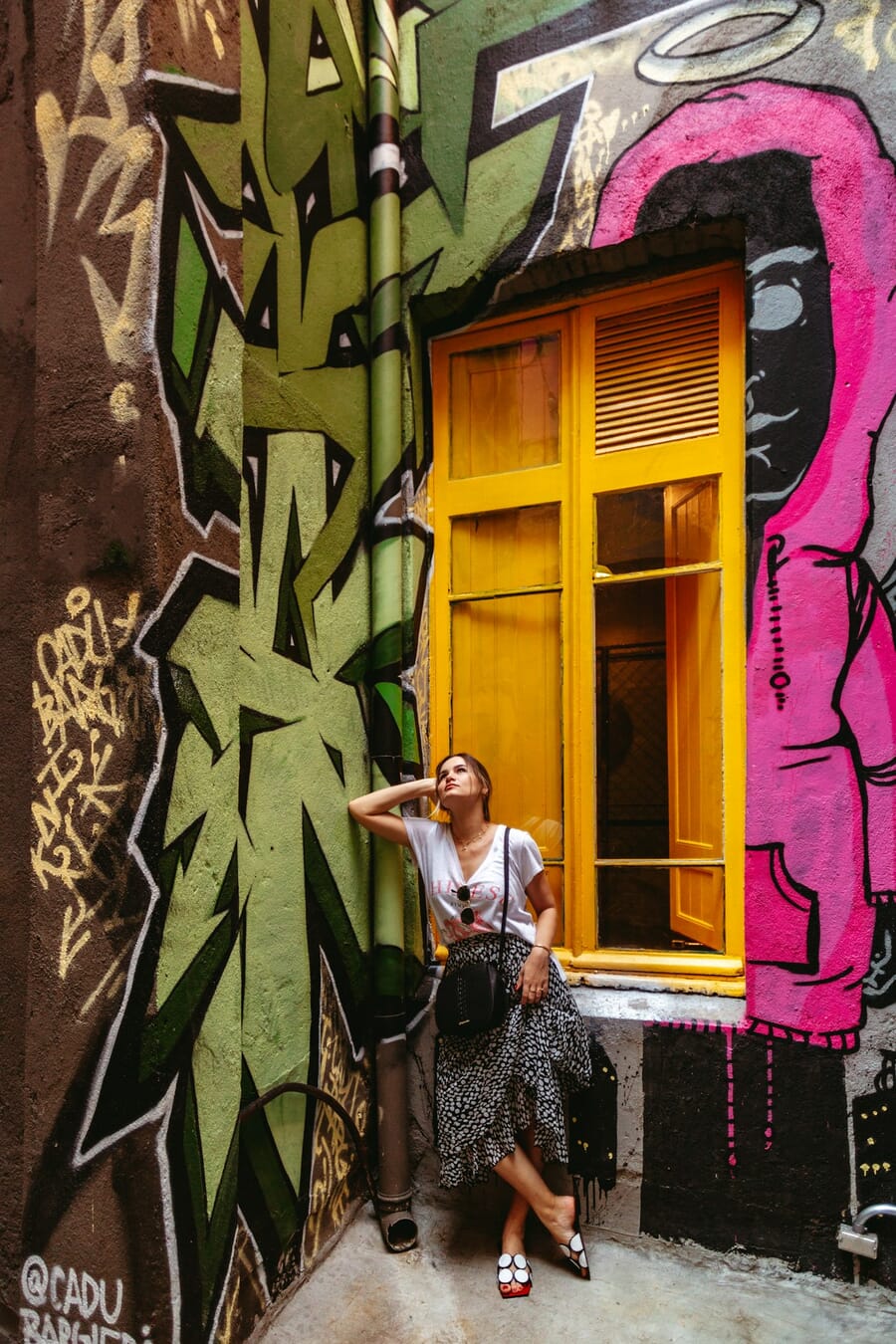Woman leaning her back against a graffiti wall in a casual relaxed pose with one leg bent