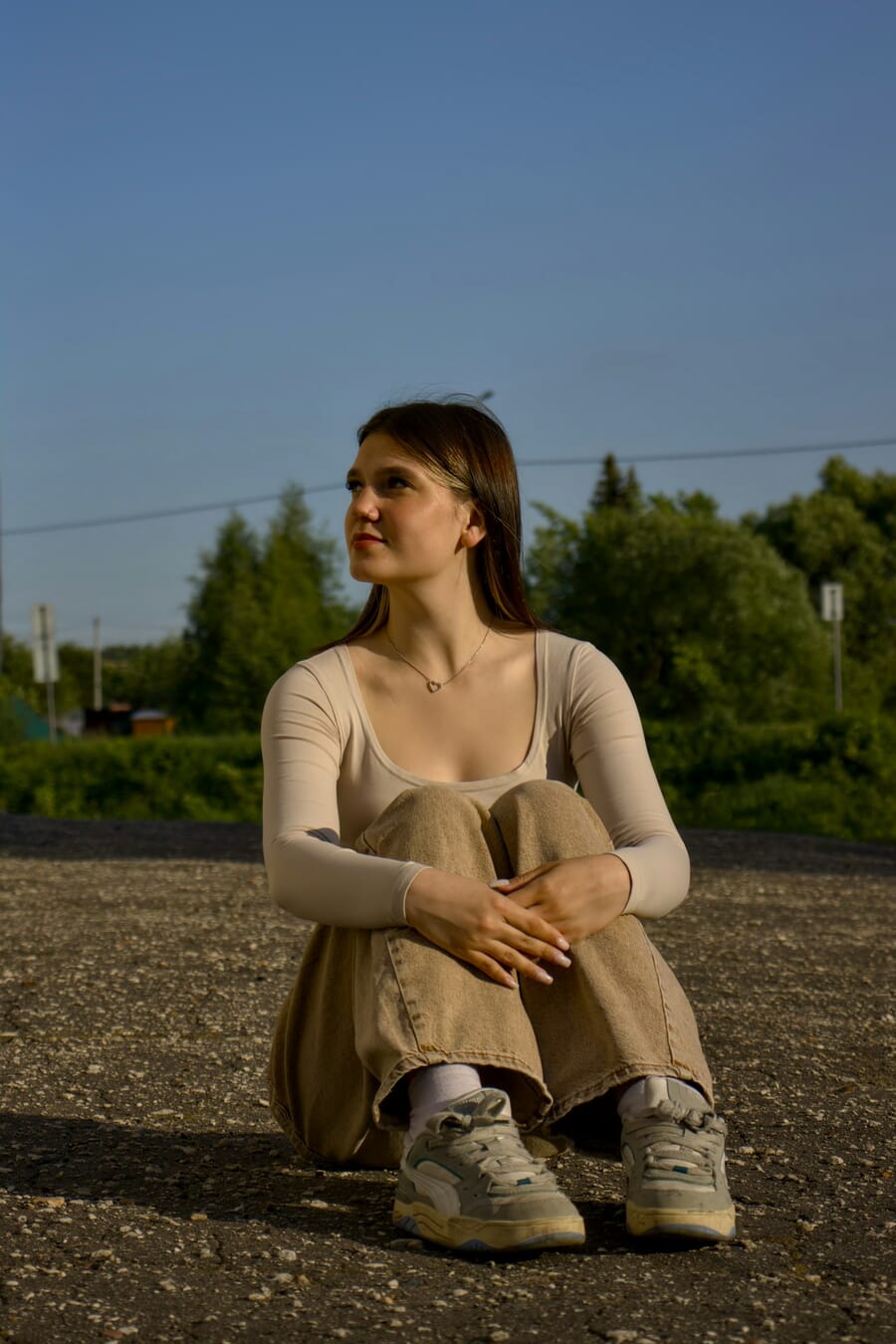 Woman sitting on the ground with knees drawn up and arms wrapped around her knees in a cozy compact pose