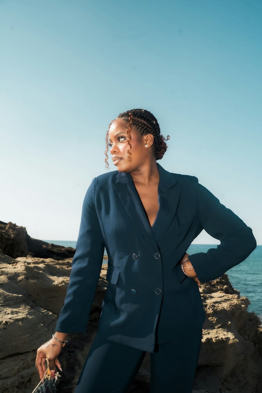 Woman in a navy suit standing confidently with one hand placed on her hip near the beach