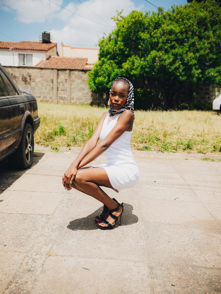 Young woman in a white dress squatting outdoors in a confident low pose