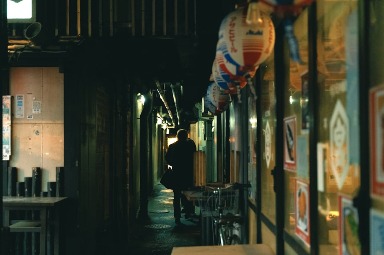 A figure walking through a narrow urban alley with strong diagonal perspective