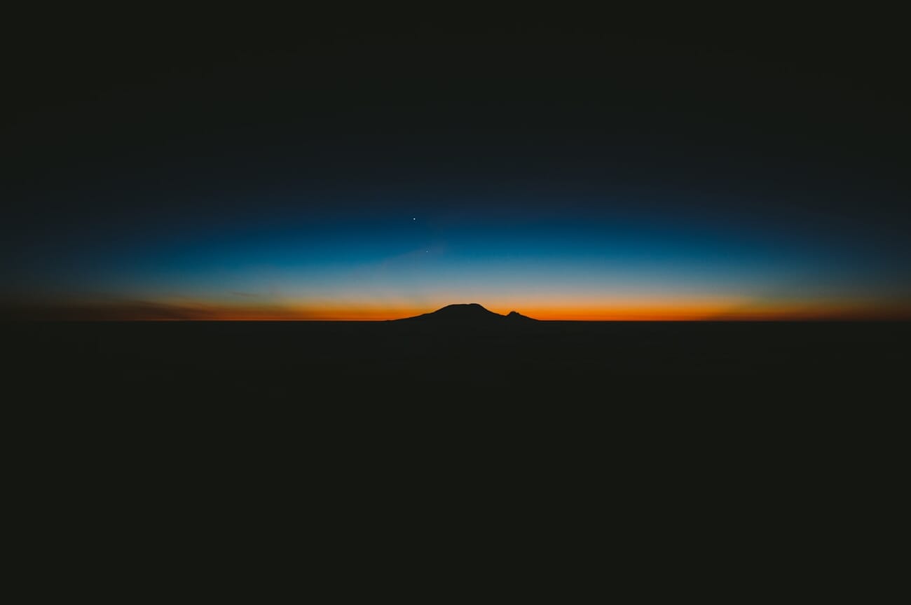 Silhouette of a person against bright twilight sky over mountain peaks