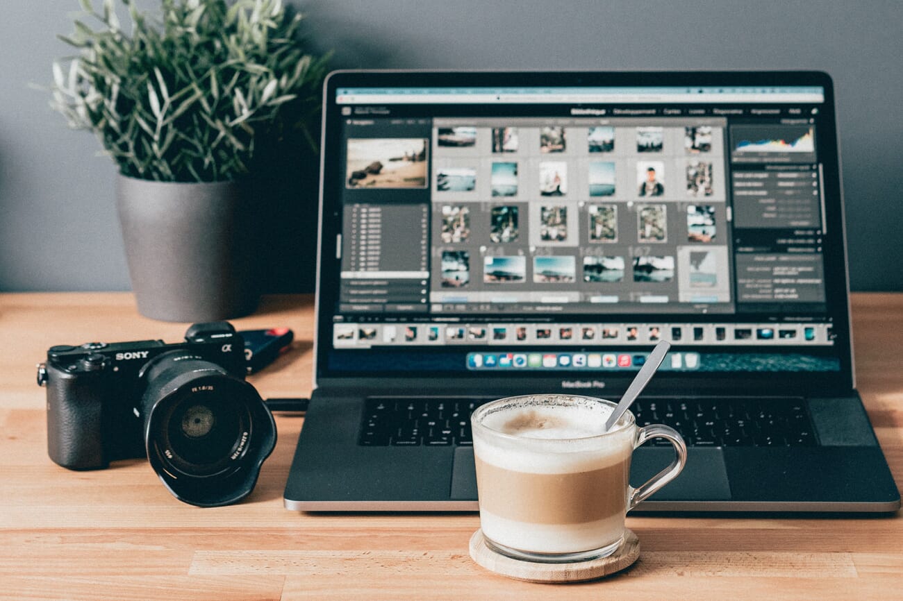 A coffee cup in front of a Sony mirrorless camera and a MacBook Pro running Lightroom Classic