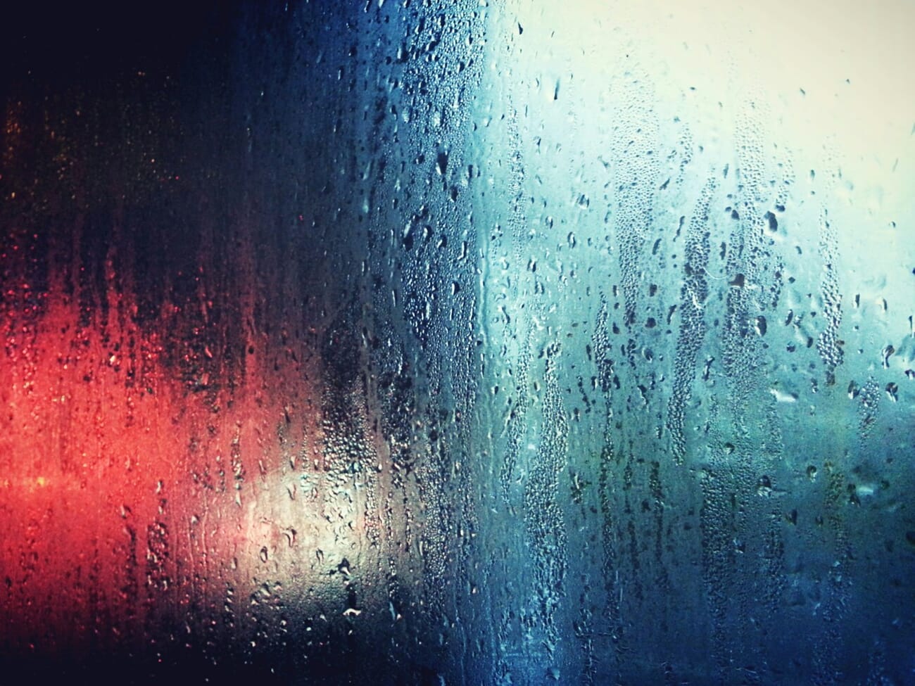 Photograph of a rainy window with water droplets in focus and blurred world beyond