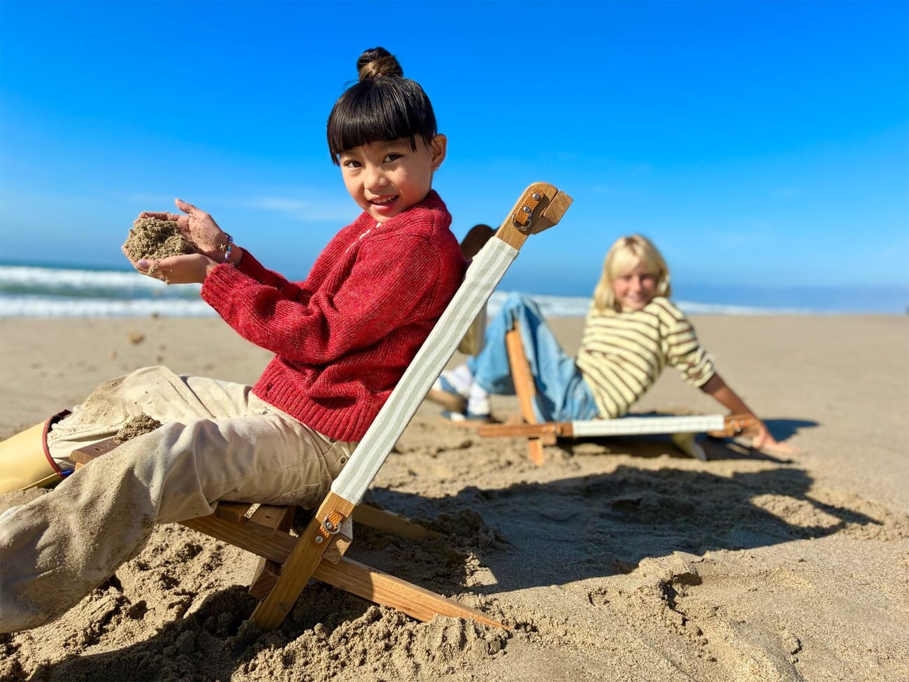 iPhone 17e sample portrait mode photo of two children on a beach, one with camera equipment, showing shallow depth of field