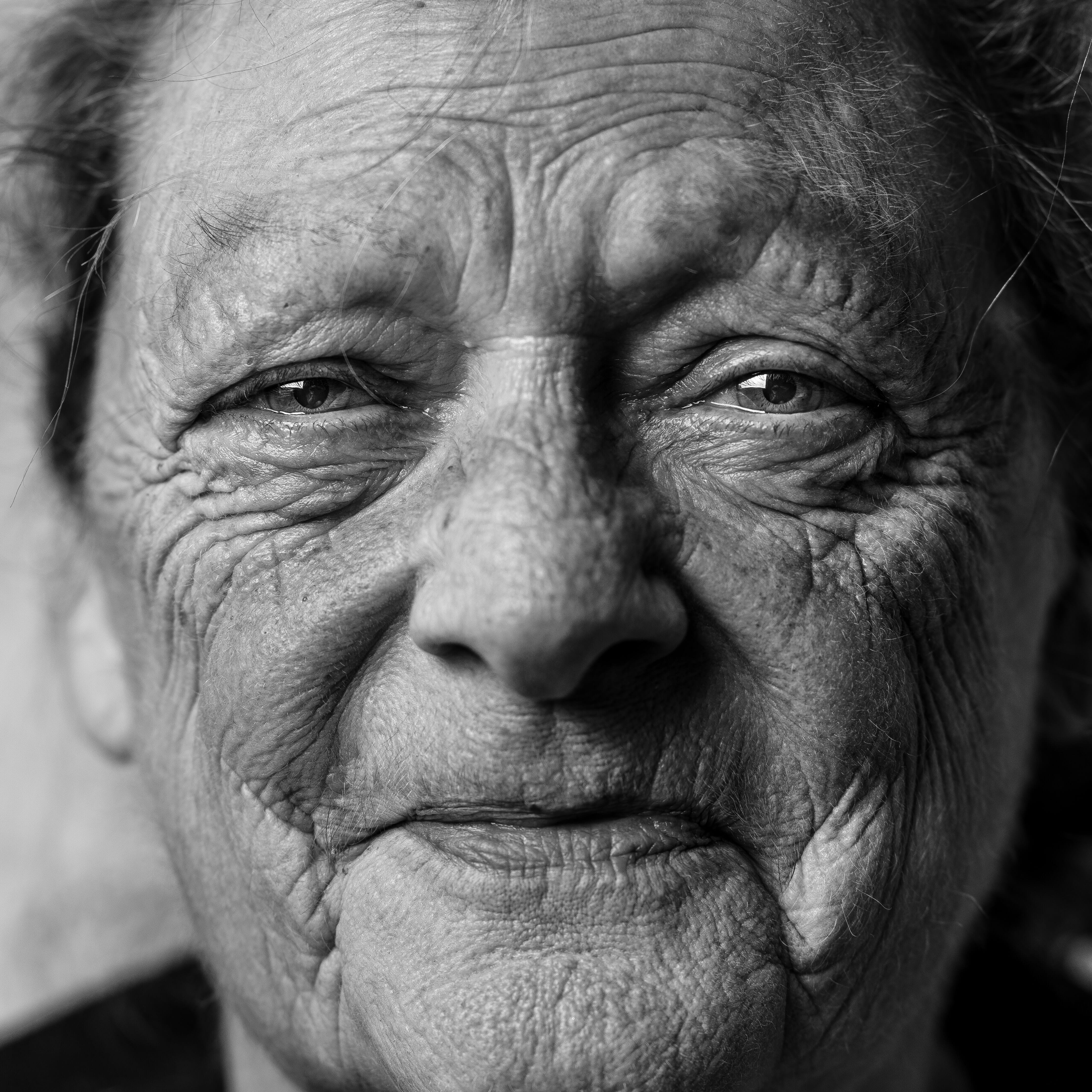 Close-up of an old woman with heavy wrinkles with a sad smile in black and white.