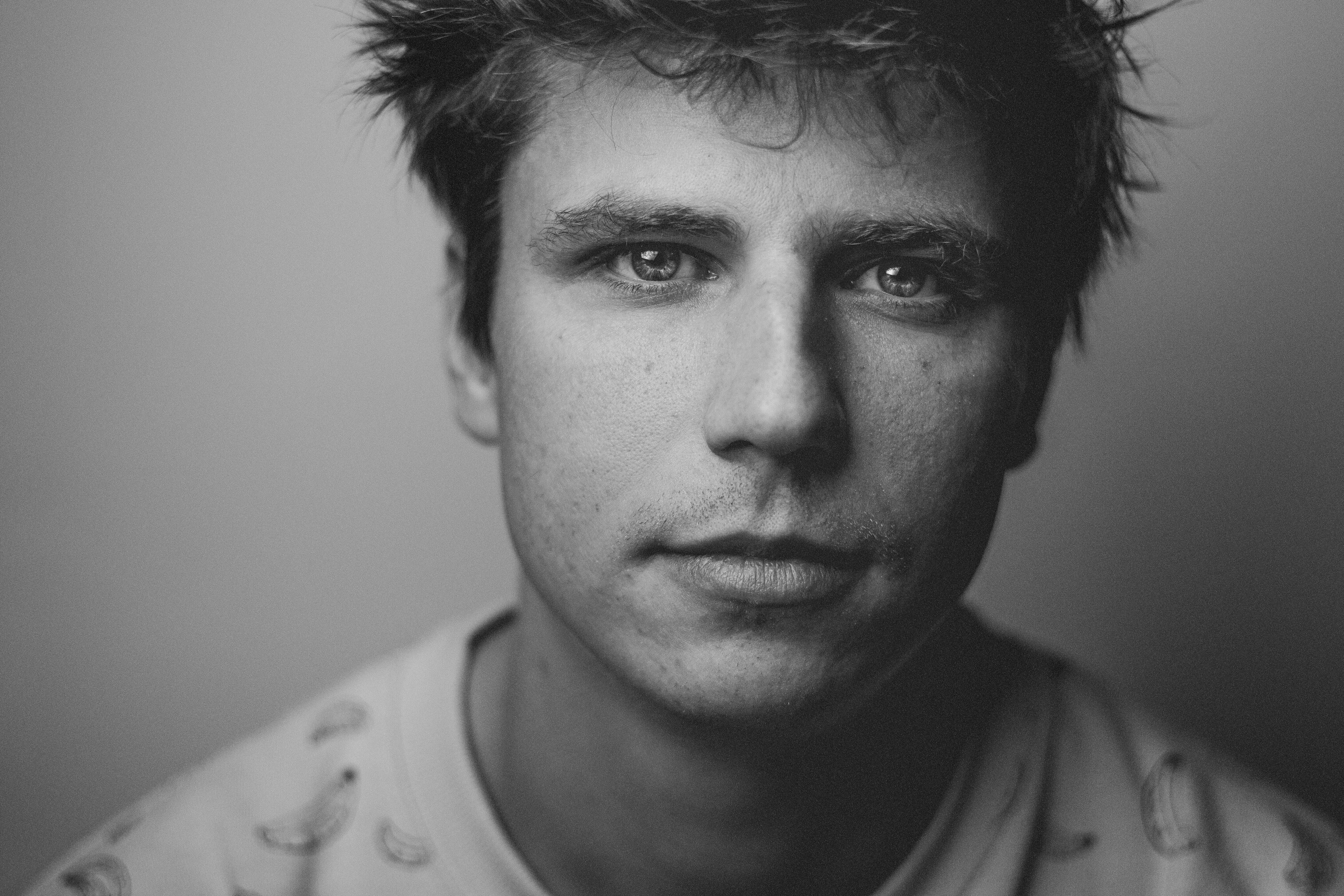 Headshot of a man looking straight ahead with messy hair on a neutral background in black and white.