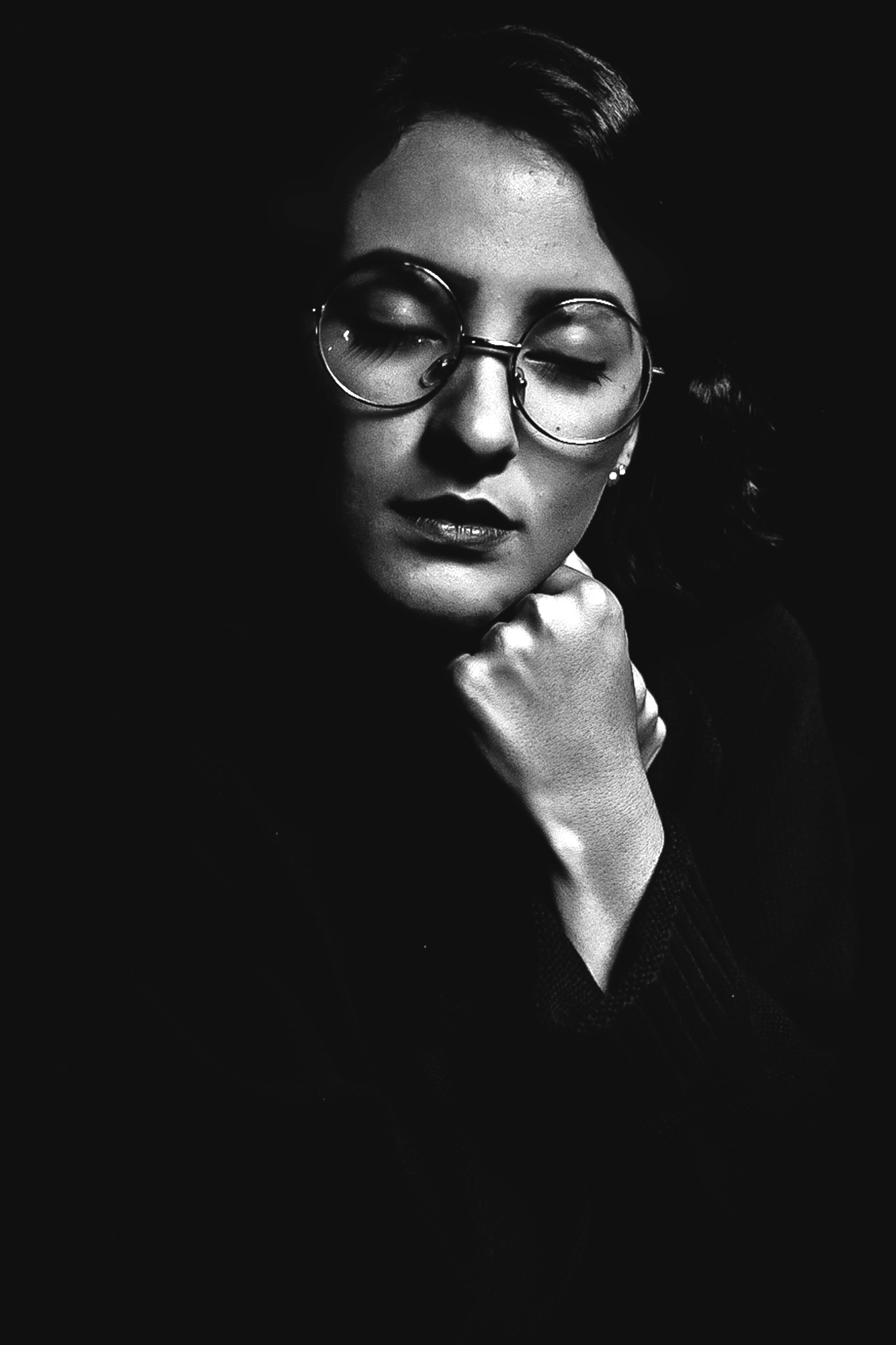 A woman with dark hair, circular glasses, and closed eyes resting her chin on a hand.