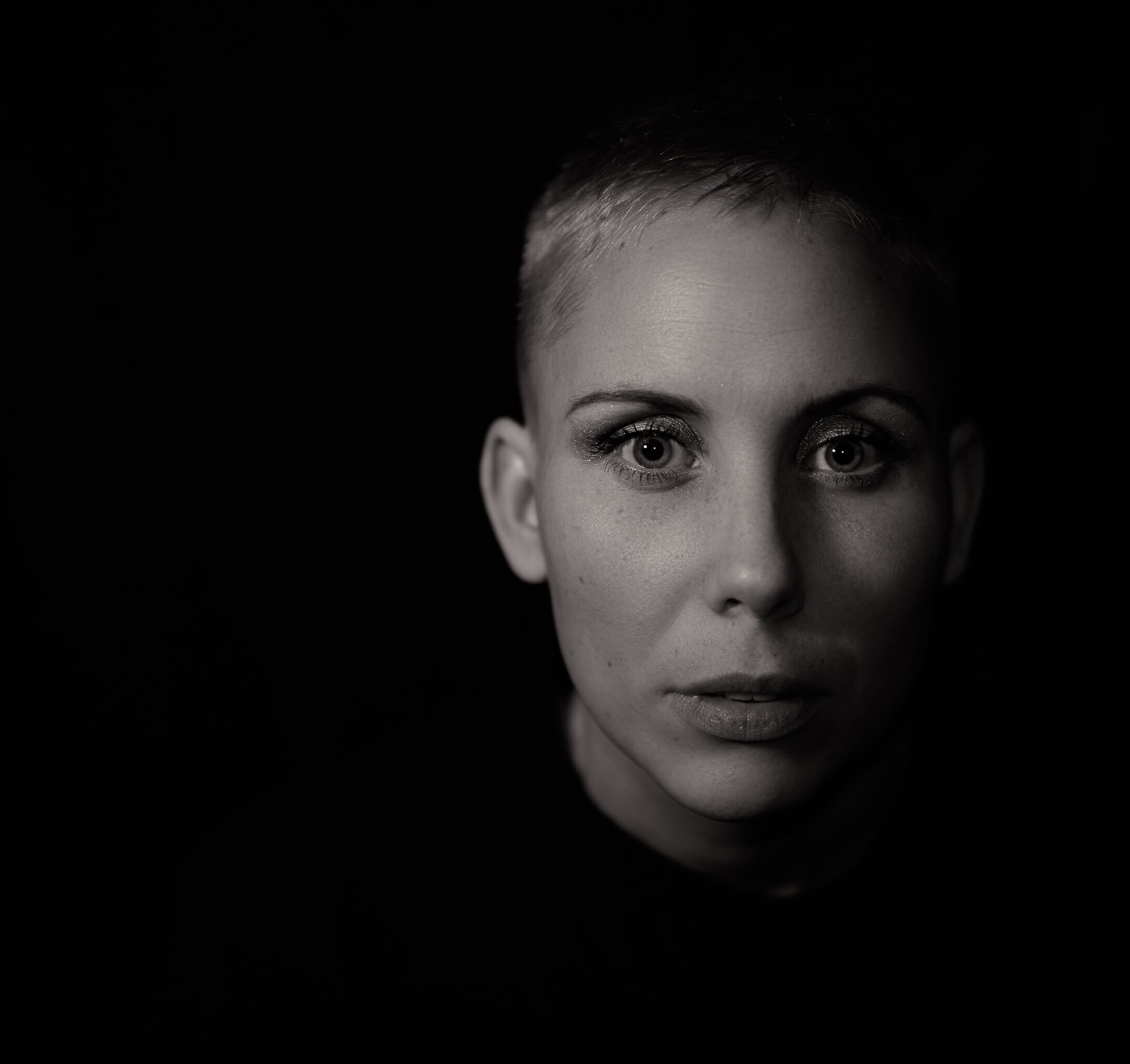 A short-haired woman with wide eyes and parted lips on a black background.