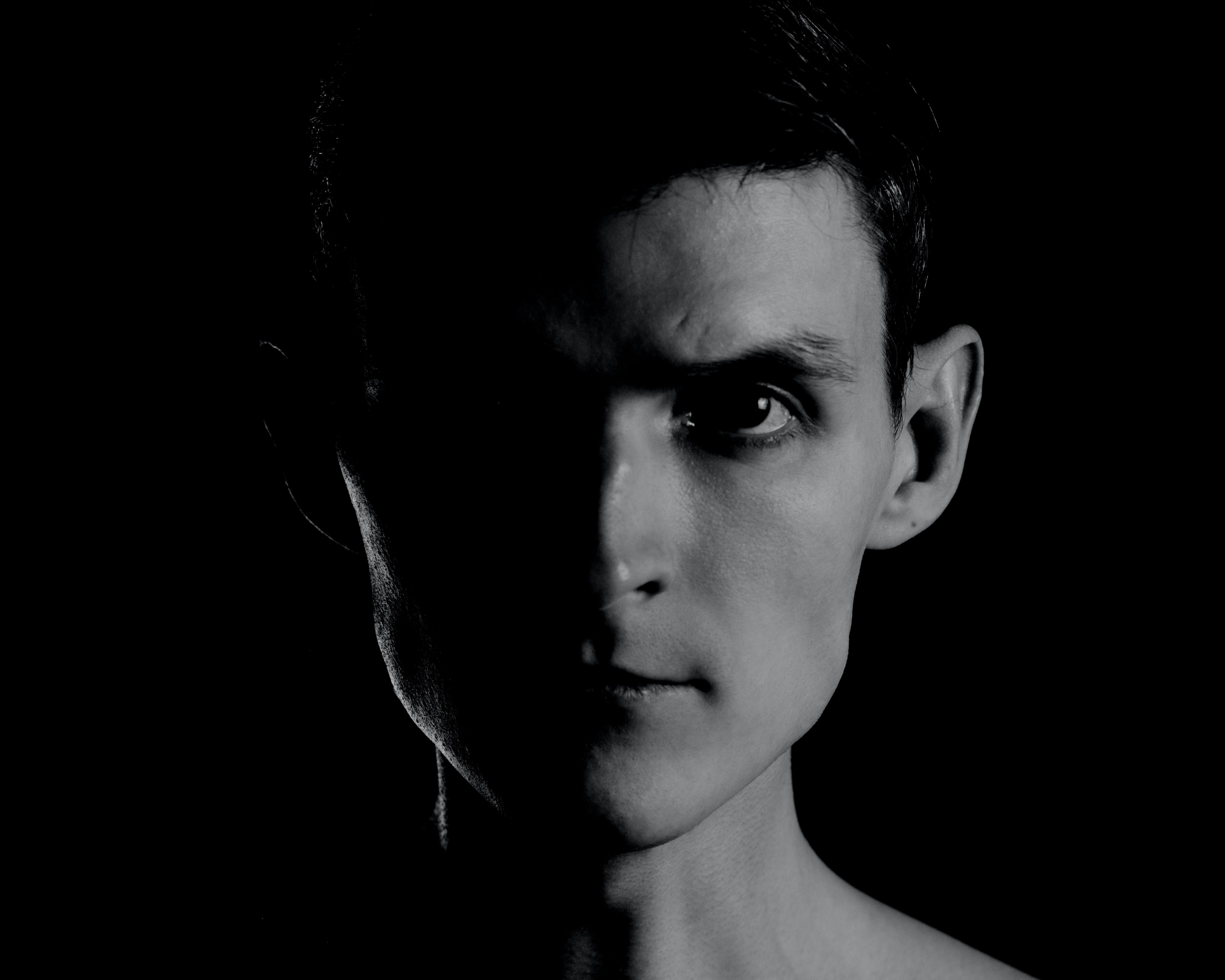 A young man with an angular jaw and an intense expression with half his face in shadow.