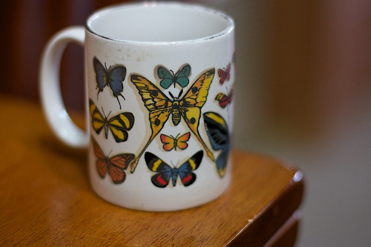 Butterfly-Patterned Coffee Mug on Wooden Table, Warm Light Revealing Colorful Wings