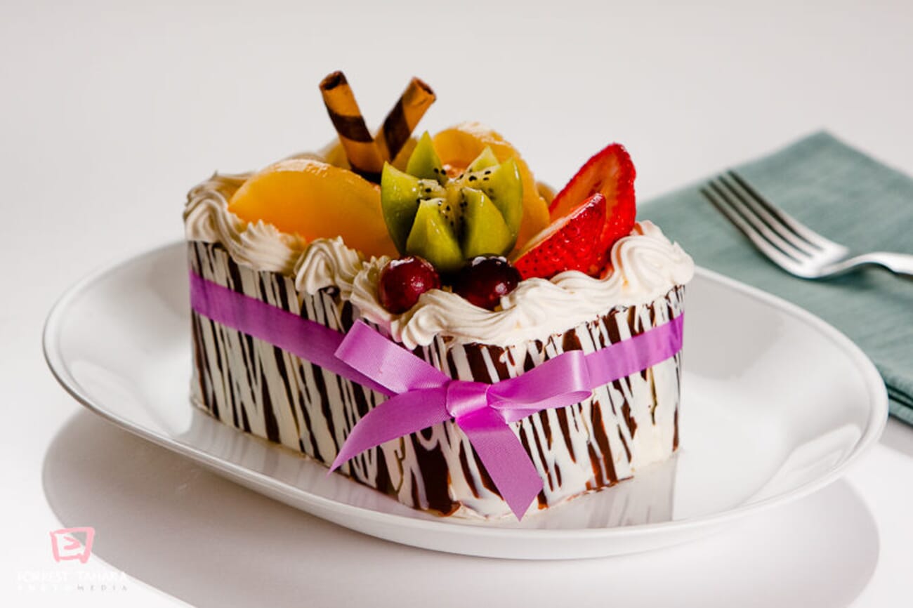 Fruit-Topped Zebra-Chocolate Cake with Purple Ribbon on White Plate