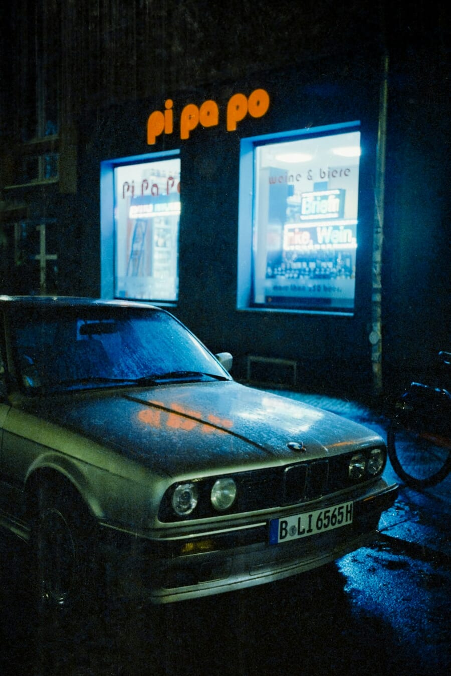 BMW E30 under blue neon reflections on rain-soaked street — shot on Minolta CLE