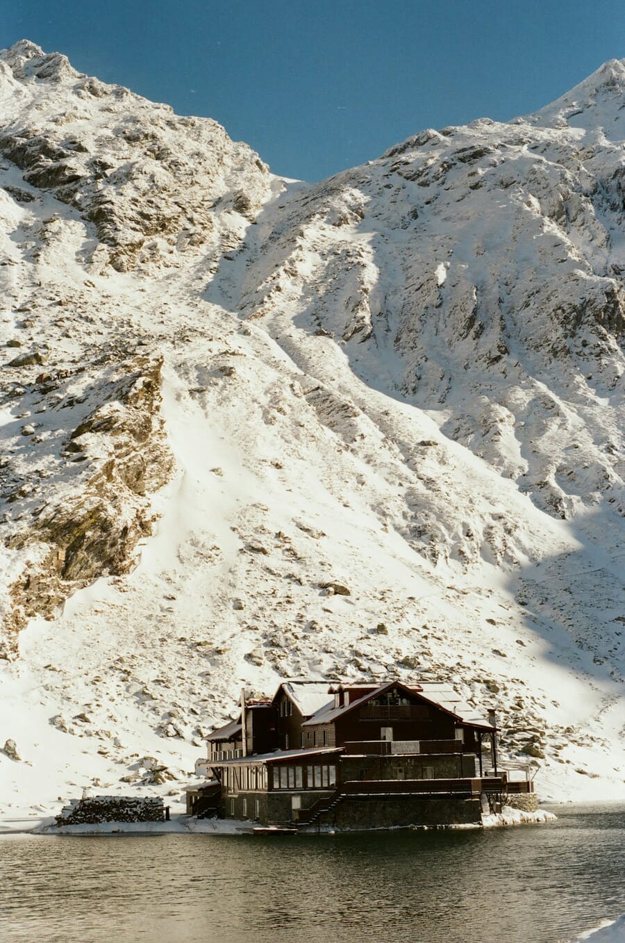 Alpine lodge on frozen lake beneath snowy cliffs — shot on Minolta XE-5