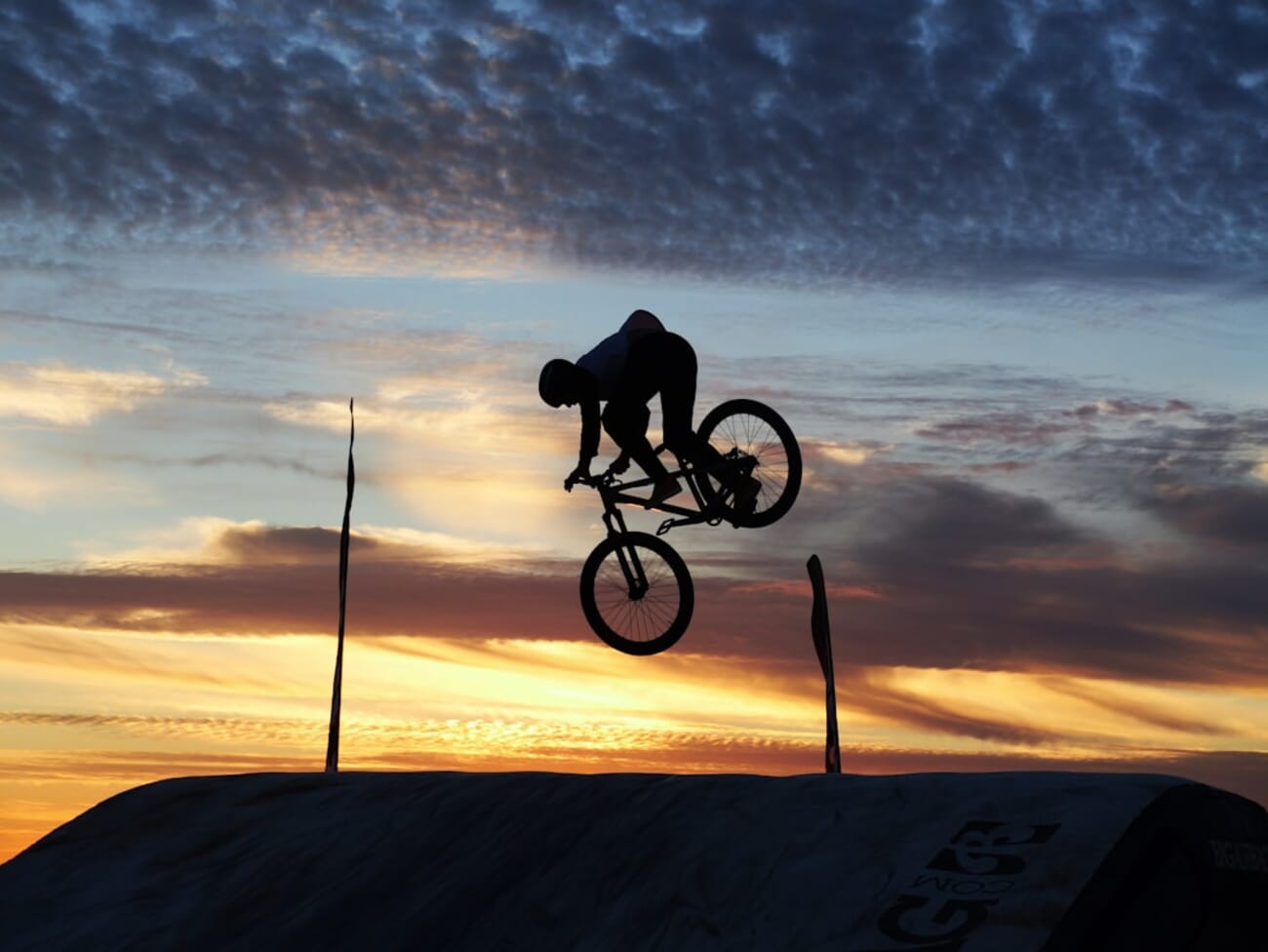 Cyclist frozen mid-jump against a sunset sky — fast shutter speed freezes the action