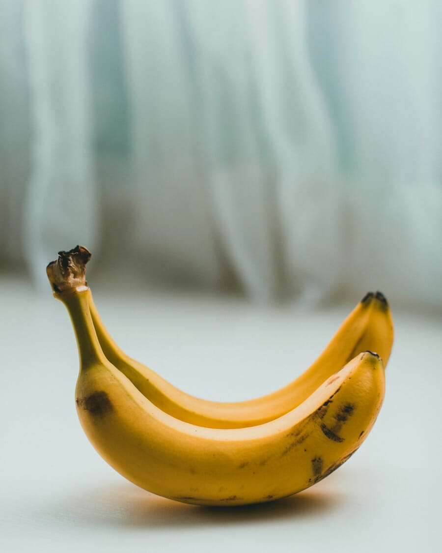 Original Unsplash photo of two bananas on draped blue-gray textile with visible fabric folds and shadows