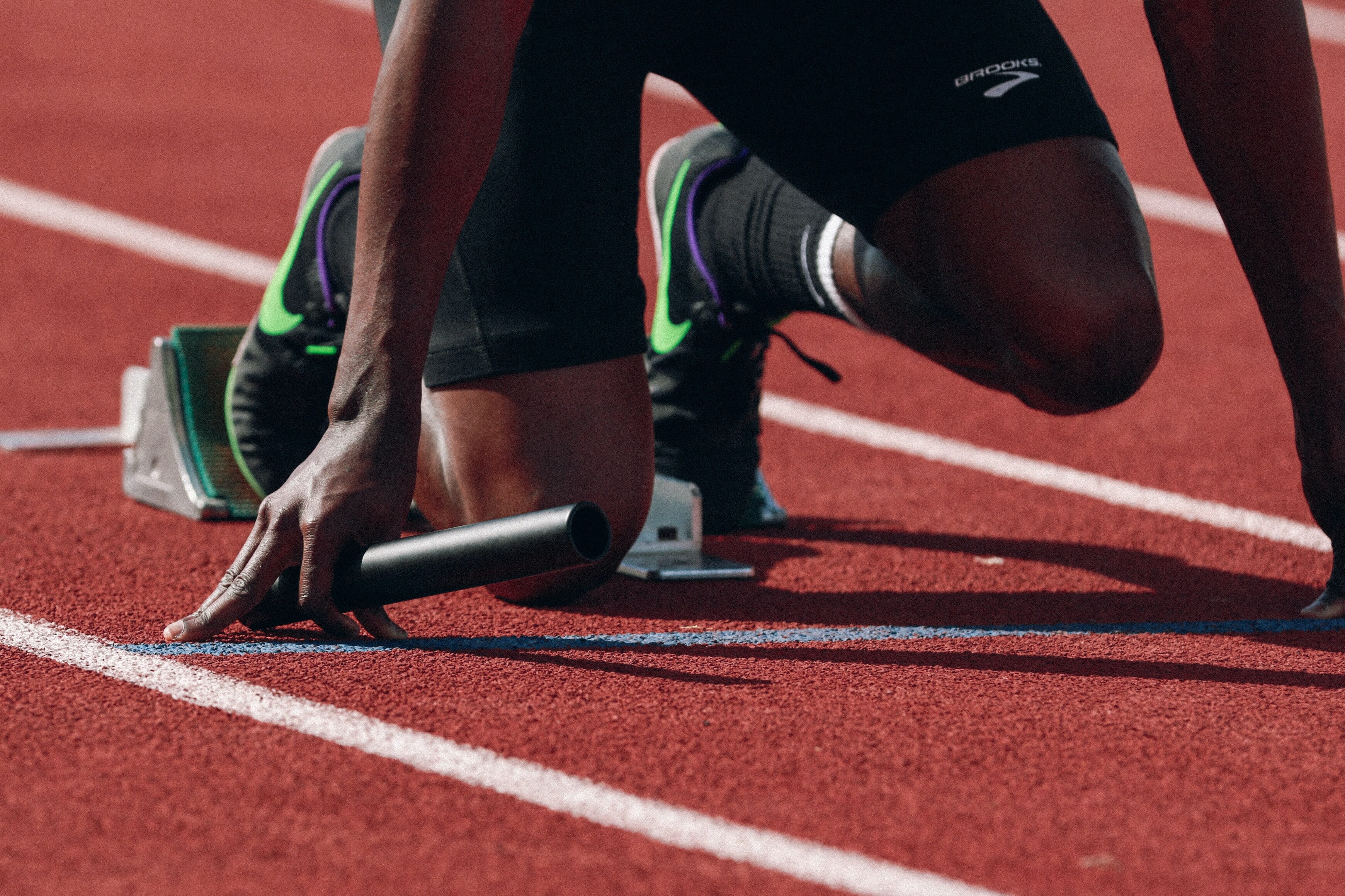 A close-up of a runner's feet and a hand holding a baton on a red track.