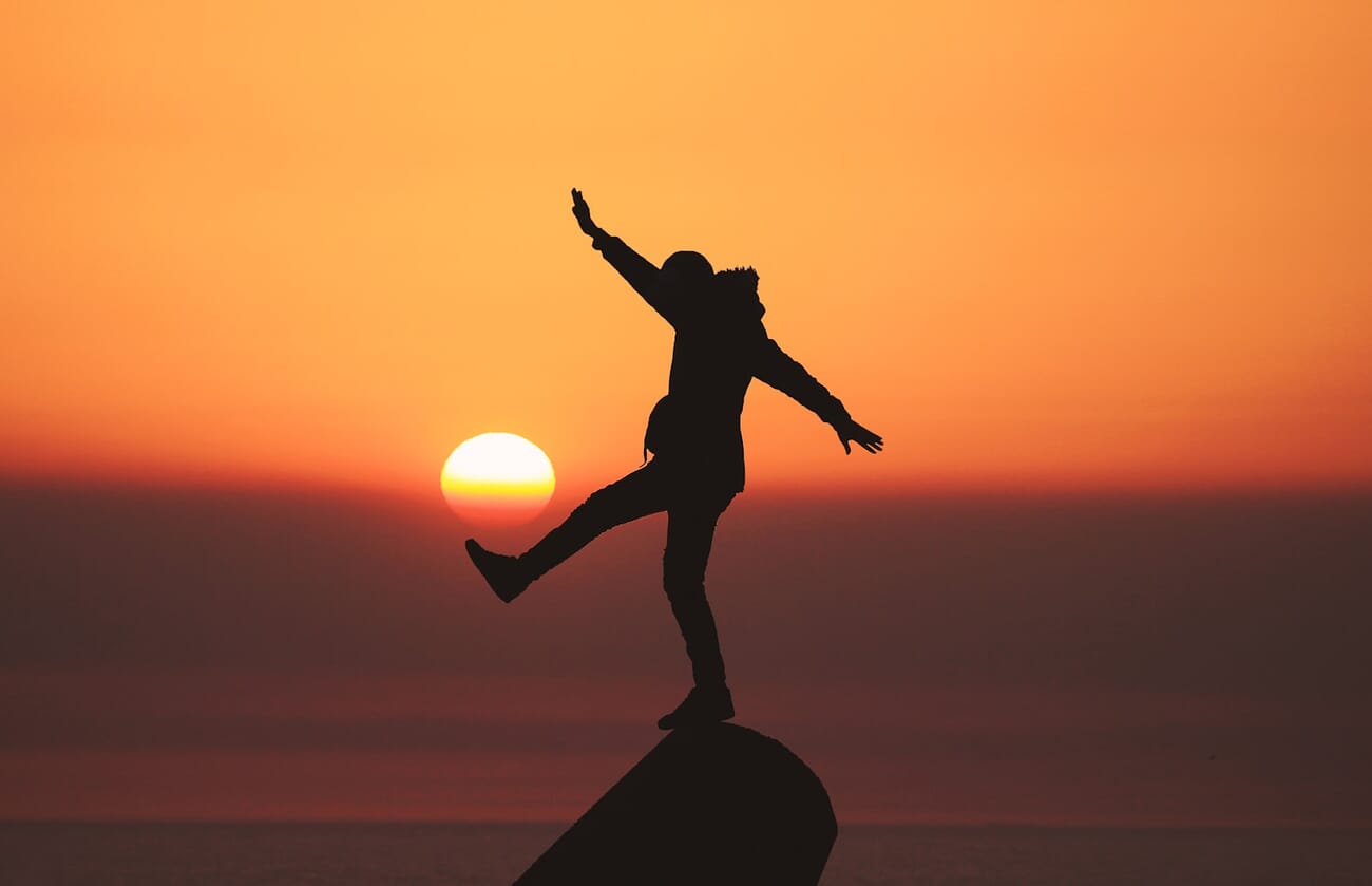 Silhouette of person balanced on a rock during golden hour sunset