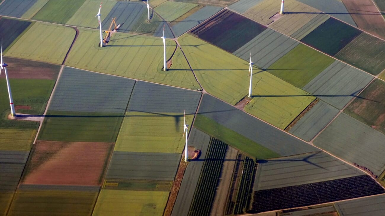 Aerial view of wind turbines casting long dramatic shadows across farmland at sunrise