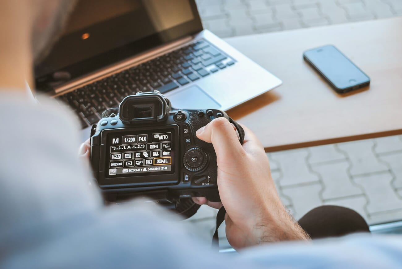 A photographer setting up a shot at a creative workspace, camera gear and notebooks on the table, shot at f/4.5 · 1/30 · ISO 100