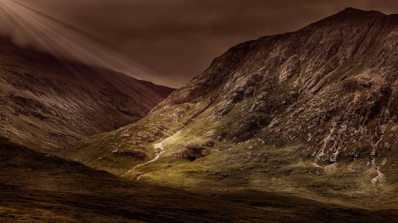 A dramatic mountain valley lit by low sunlight, rocky foreground and peaks sharp from edge to horizon, shot at f/6.3 · 1/250 · ISO 100