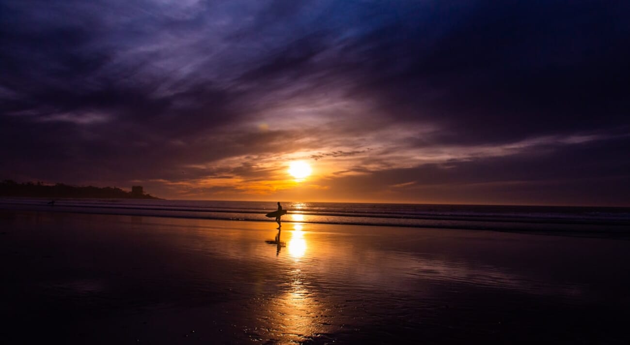 Silhouette of a surfer holding a surfboard on the shore at sunset