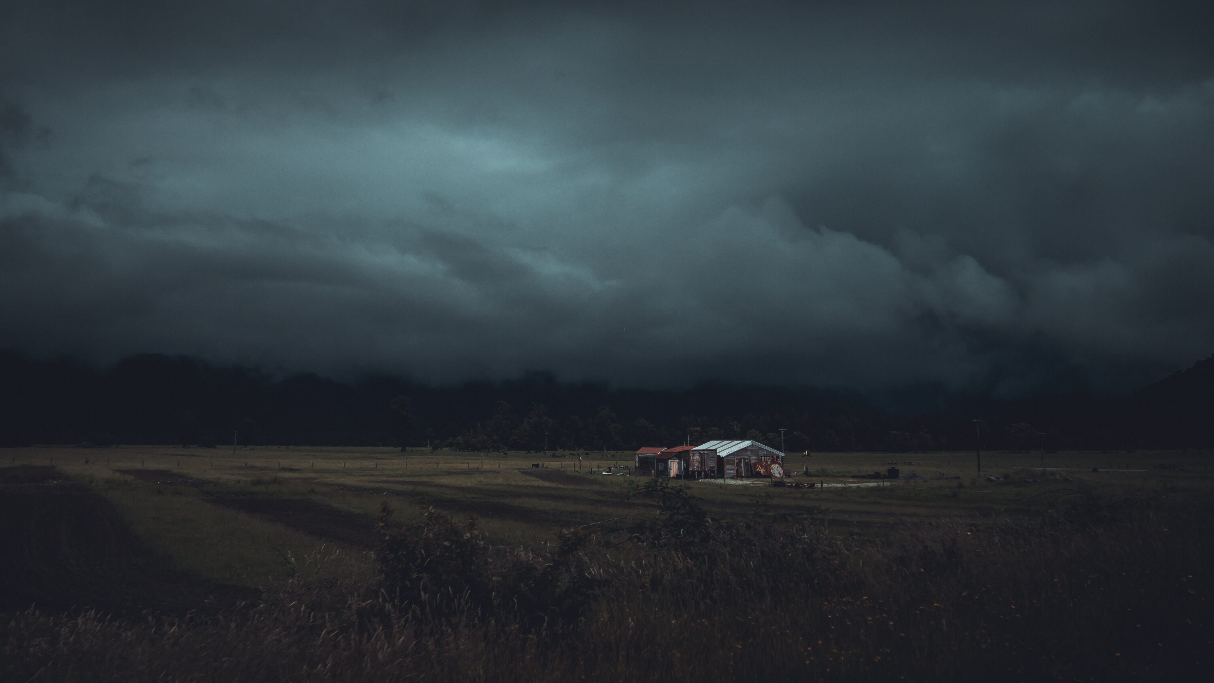A farmhouse underneath dark, stormy skies surrounded by an expanse of grassy land.