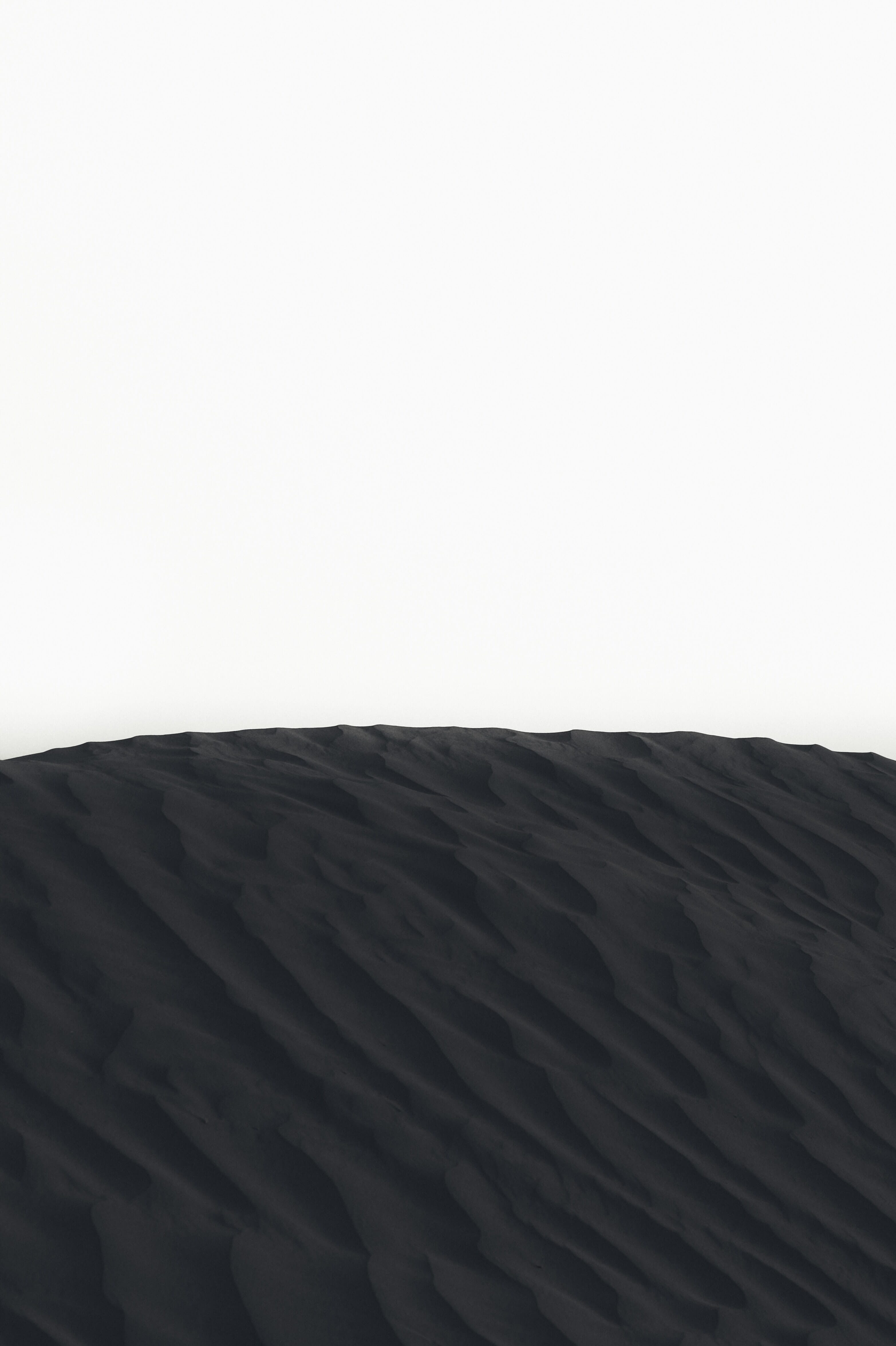 A black and white close-up of a sand dune ridge framed against a white sky.