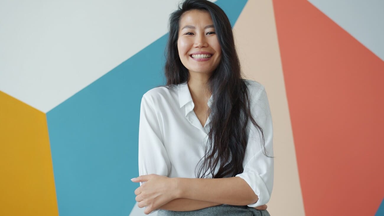 Smiling woman in white shirt posing against a colorful geometric studio backdrop