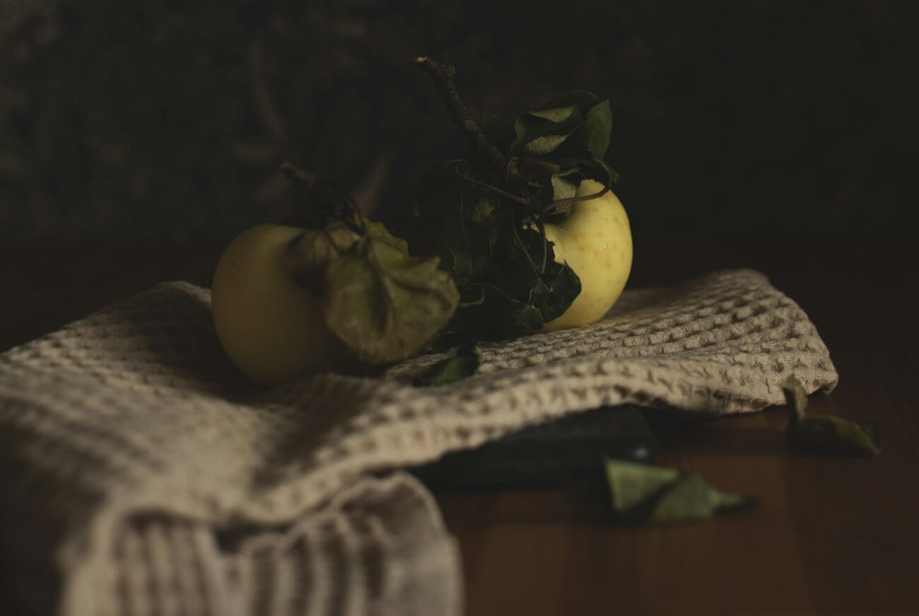 Dark moody still life photograph of apples on a table with dramatic lighting