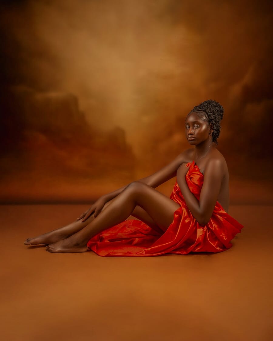Woman draped in flowing red fabric against a warm studio backdrop