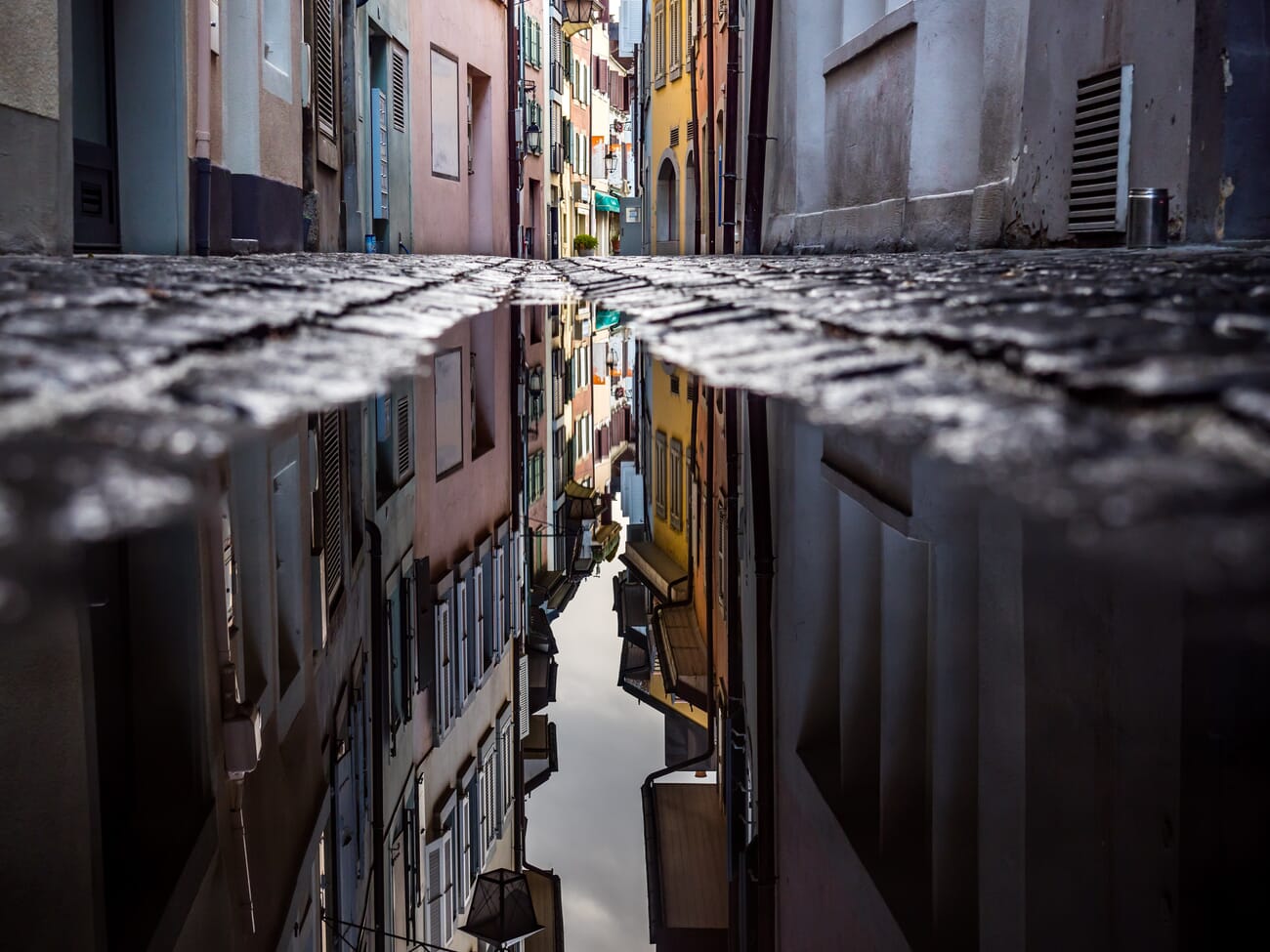 A narrow alley shot from a low angle and reflected in a cobblestone puddle