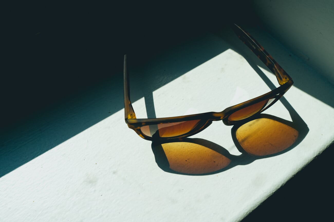 Yellow-brown sunglasses on a bright green ledge casting a strong shadow