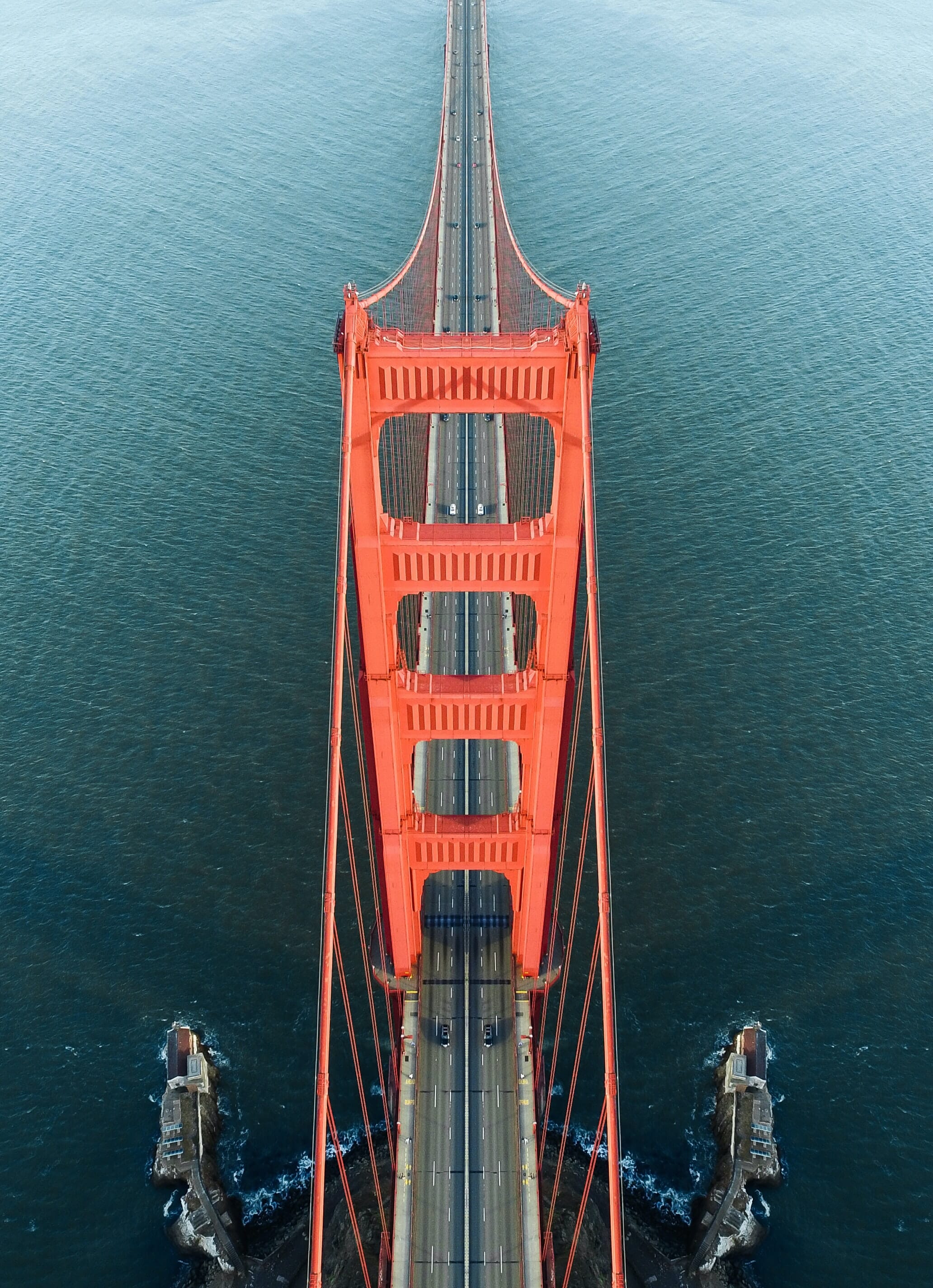 An aerial of a red bridge over turquoise water with cars cruising down below.