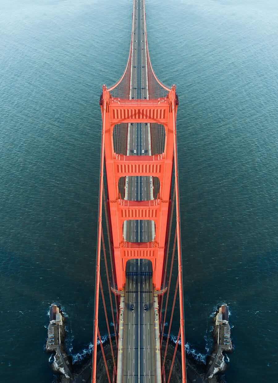 Aerial of a red bridge over turquoise water with cars below