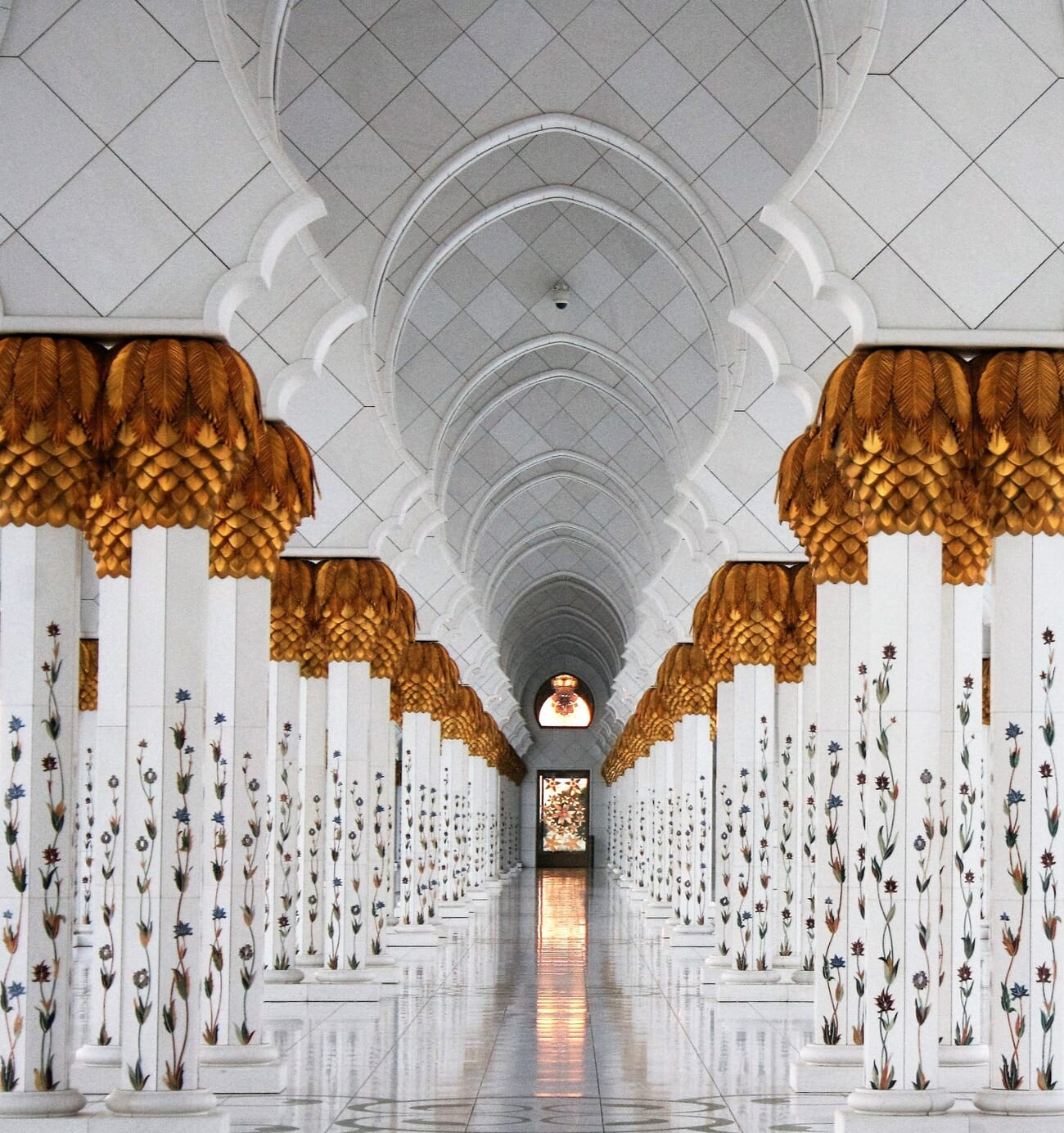 Symmetrical columns and arches of a white building leading toward a distant door