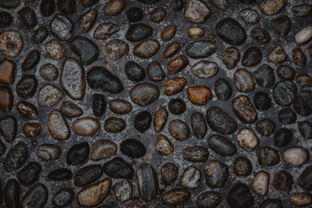 Smooth river pebbles embedded in dark cement showing textural contrast