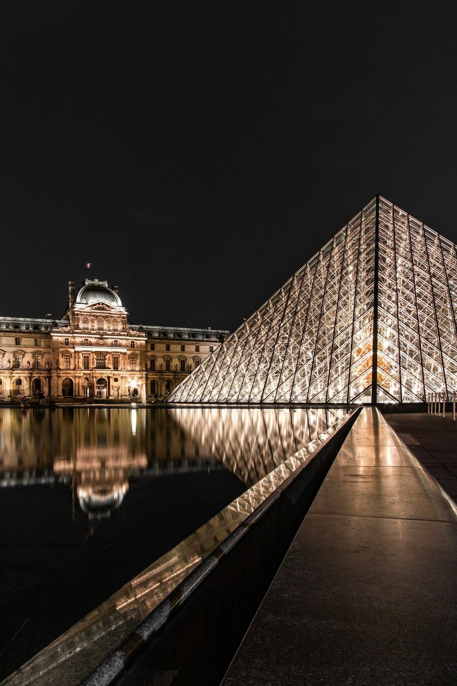 The Louvre glass pyramid at night, a monumental architectural triangle with its reflection