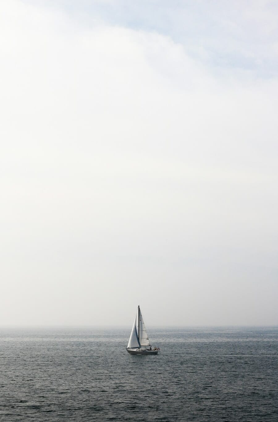 Sailboat with a triangular sail on a calm sea, a literal triangle shape carrying the composition