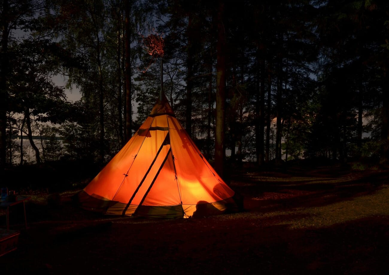 Glowing tipi forming a symmetrical triangle in a dark forest at night