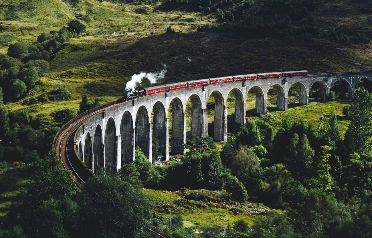 Steam train crossing a curved viaduct, forming irregular dynamic triangles with the hillside
